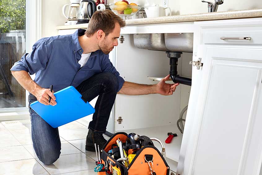 Housing inspector inspecting the plumbing under the kitchen sink.
